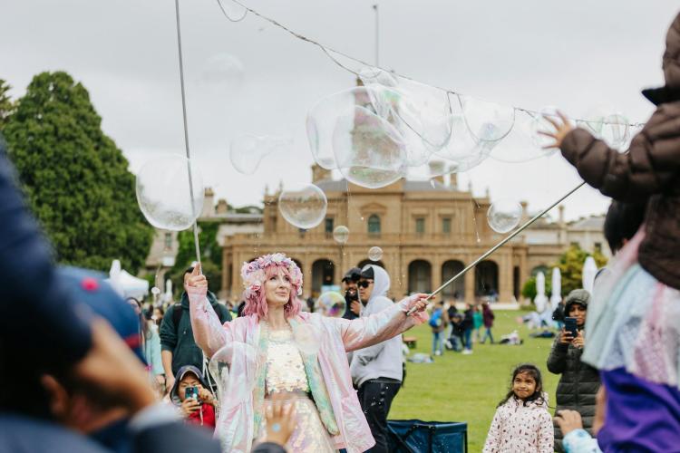 a performer dressed in pink blowing bubbles in front of Werribee Park Mansion